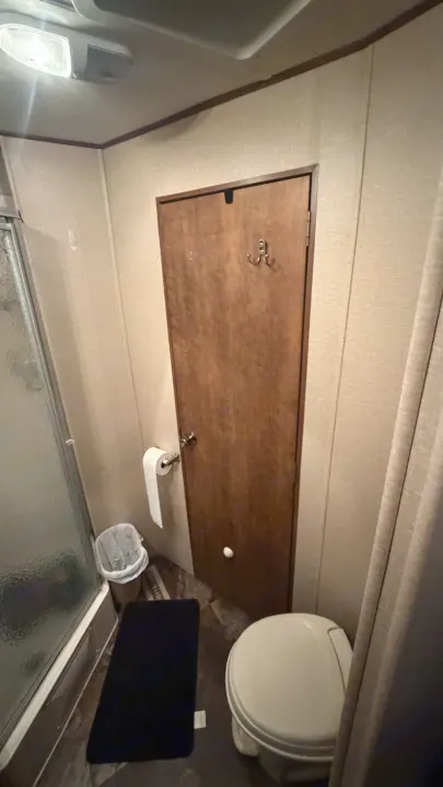 Compact RV rental bathroom with shower, toilet, and narrow door with hooks. Efficient design for travel.. Crossroads RV Rezerve 2015