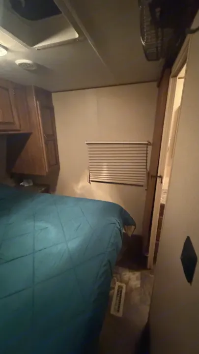 Inside an RV rental: a cozy bedroom features a blue quilted bed, wood cabinets, window blinds, & a ceiling fan.. Crossroads RV Rezerve 2015