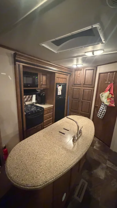 This RV rental kitchen features a speckled island with a sink, stove, microwave, and wood cabinets. Compact yet functional.. Crossroads RV Rezerve 2015