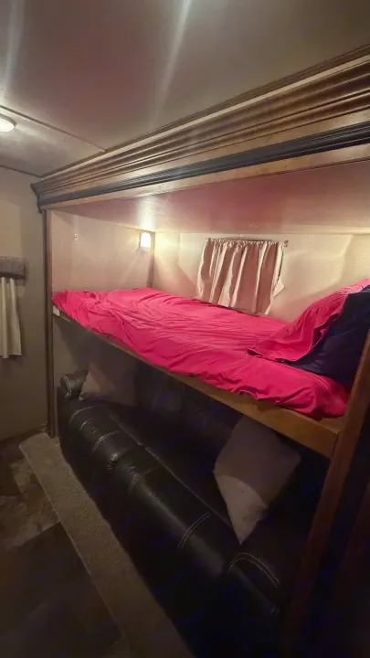 Cozy RV rental interior with a bright pink-comforter bunk bed above a dark leather sofa.. Crossroads RV Rezerve 2015