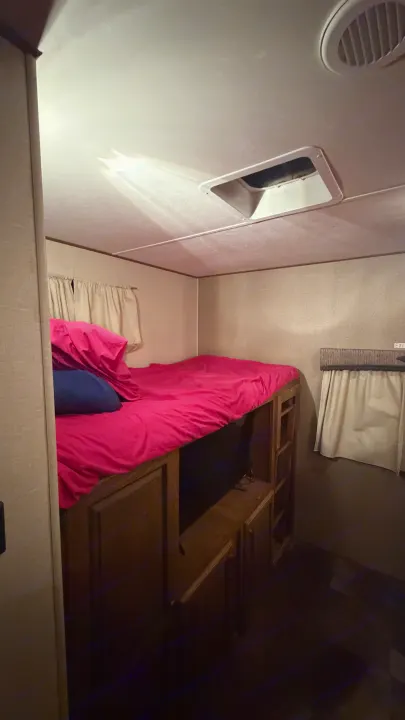 Bunk beds with pink bedding & storage in an RV rental. Includes an overhead vent, window, and exit sign for a family-friendly camper.. Crossroads RV Rezerve 2015