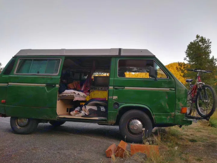 Green VW camper van with open door, interior visible, bike on back. Perfect RV rental for an outdoor adventure.. Volkswagen Vanagon 1984
