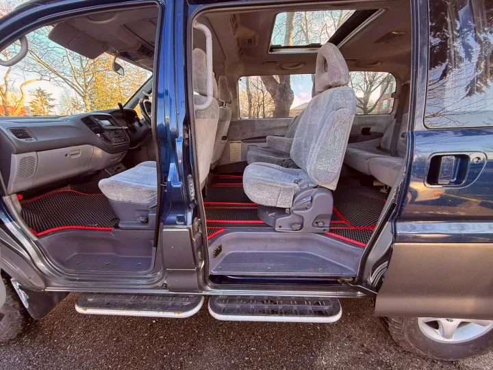 Spacious RV rental interior with open doors, gray fabric seats, black/red floor mats, and open sunroofs for a bright cabin.. Mitsubishi Delica 2000