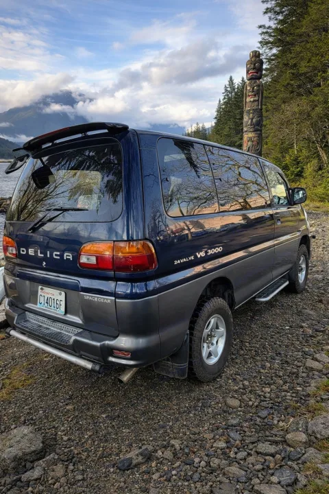 Dark blue Mitsubishi Delica Space Gear 4x4 van, ideal for rv rental, parked by a lake with mountains & a totem pole.. Mitsubishi Delica 2000