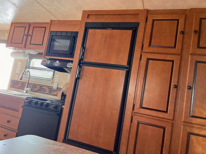 An RV rental kitchen featuring a Dometic fridge, Magic Chef microwave, wood cabinets, sink, and stove. Ready for trips!. Forest River Palomino Canyon Cat 2014