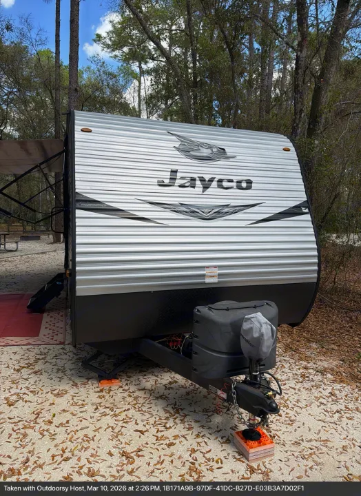 Enjoy this Jayco RV rental, a silver travel trailer with an extended awning, parked at a leafy campsite.. Jayco Jay Flight SLX 2021