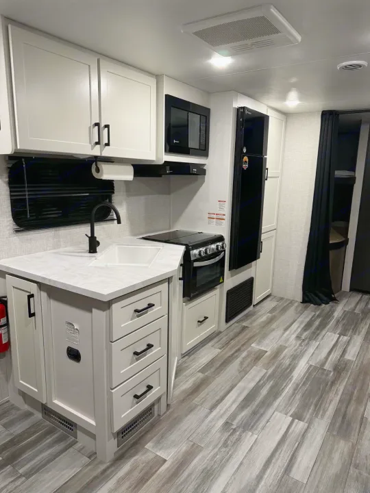 Stylish RV rental interior: a fully equipped kitchen with white cabinetry, black appliances, sink, and wood-look flooring.. Jayco Jay Flight SLX 2025