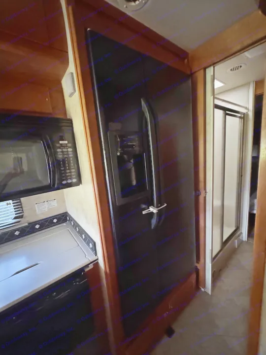 RV rental kitchen view: black microwave, large fridge with dispenser, counter, & a shower area seen in the background.. Gulf Stream Tour Master 2007