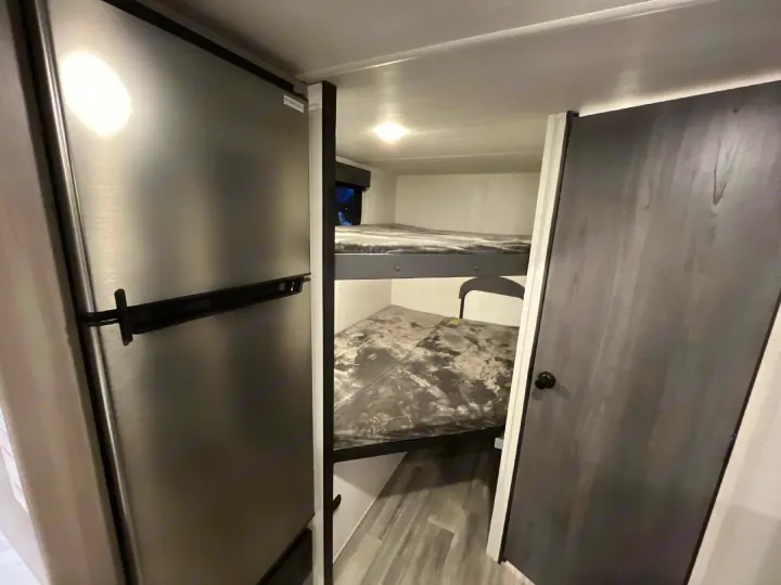 Compact RV rental interior featuring a stainless steel fridge and cozy bunk beds. Ideal for family travel adventures!. Keystone RV Hideout Sport 2024