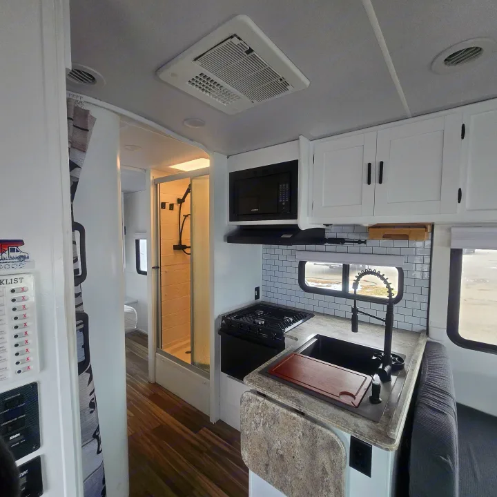 This rv rental features a bright interior with a compact kitchen (microwave, stove, sink, subway tile backsplash) and an adjacent shower stall.. Forest River Coachmen Freelander 2017
