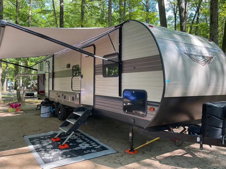 Forest River Wildwood RV rental at a shaded campsite with awning extended, steps to an outdoor mat.. Forest River Wildwood 2020