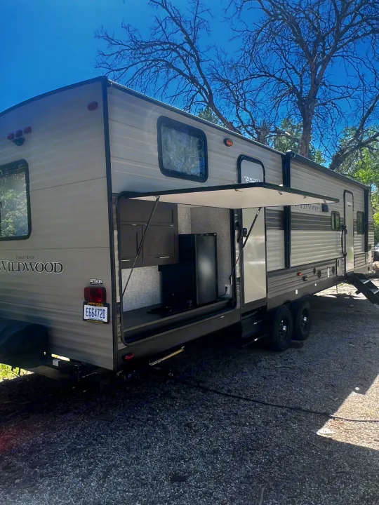 An RV rental, a Forest River Wildwood travel trailer, parked on gravel with its outdoor kitchen open, ready for camping fun.. Forest River Wildwood 2020