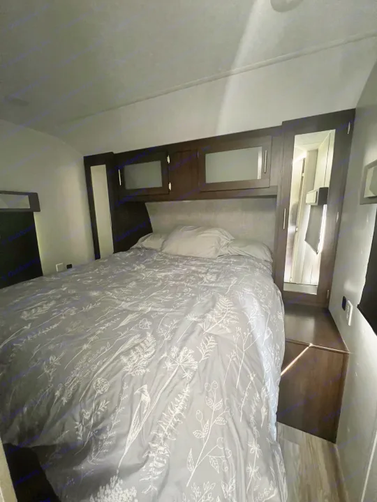 Cozy RV rental bedroom featuring a patterned duvet, overhead storage, and a mirrored wardrobe for comfortable travel.. Forest River Wildwood 2020