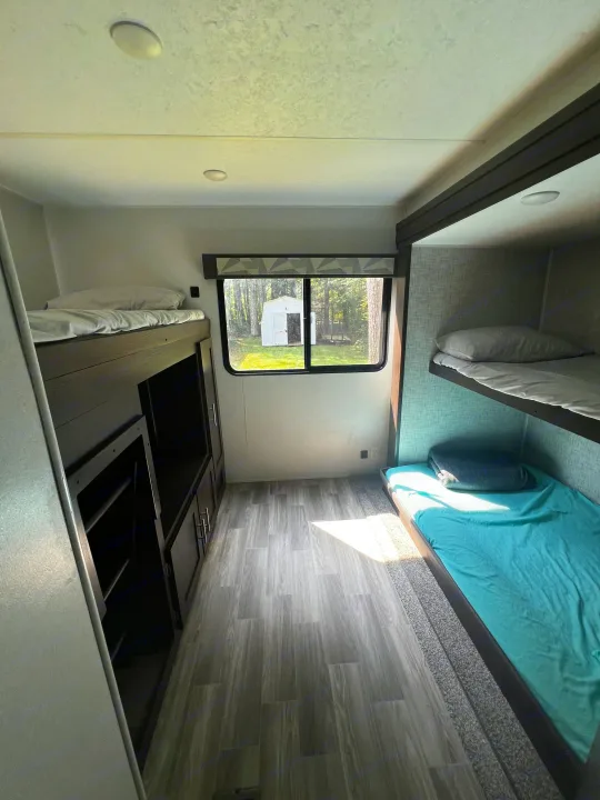 Inside an RV rental: a bright bunkhouse with comfortable beds, storage, and a view of nature outside the window.. Forest River Wildwood 2020