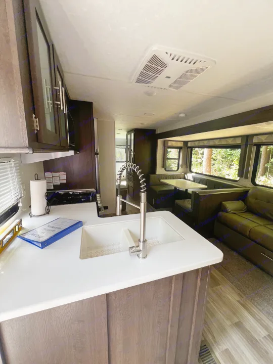 RV rental interior showcasing a clean kitchen, dining booth, and living area with scenic outdoor views.. Forest River Wildwood 2020