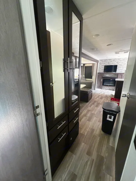 Inside an RV rental: a modern living space with a dark wood corridor, dinette, kitchen view, and TV/fireplace setup.. Forest River Wildwood 2020