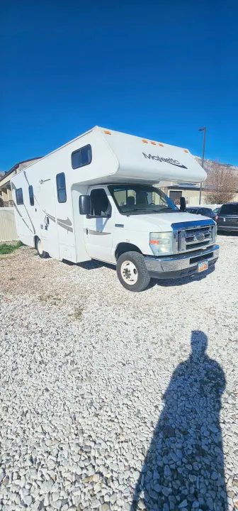 White "Majestic" RV rental parked on a gravel lot under a clear blue sky, with a visible shadow.. Thor Majestic 2014