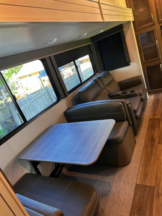 Modern RV rental interior: dining area with gray table & black benches, comfy recliner sofa by bright windows.. Keystone RV Cougar 2022