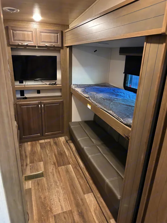 Inside this rv rental: a cozy bunk bed with a lower sofa, a mounted TV, and storage cabinets, all on wood-look flooring.. Keystone RV Cougar 2022