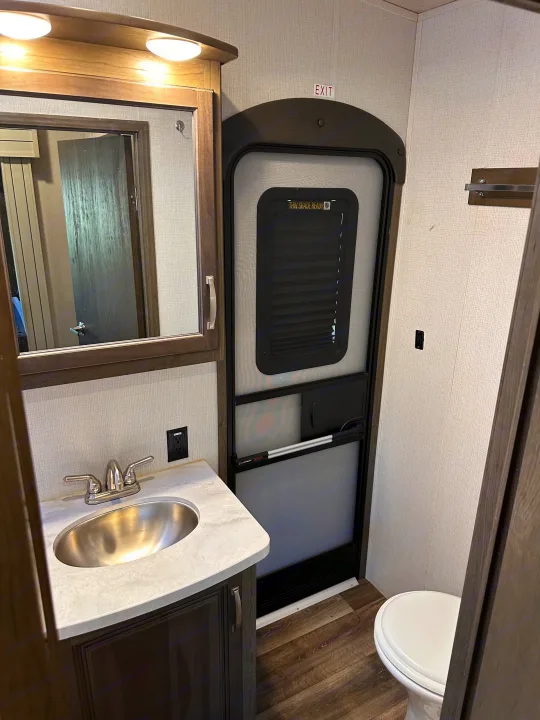 RV rental bathroom with a modern sink, mirror, partially visible toilet, and the main RV exit door featuring a screen.. Keystone RV Cougar 2022