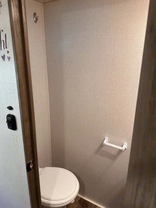 Compact RV rental bathroom with a white toilet, toilet paper holder, and wall hook on textured walls.. Keystone RV Cougar 2022