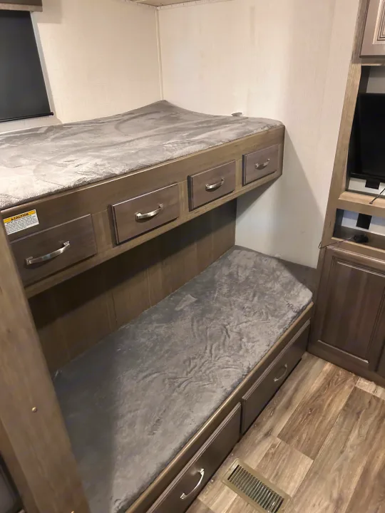 Cozy RV rental bunk beds, top and bottom, with soft grey bedding and integrated storage drawers.. Keystone RV Cougar 2022