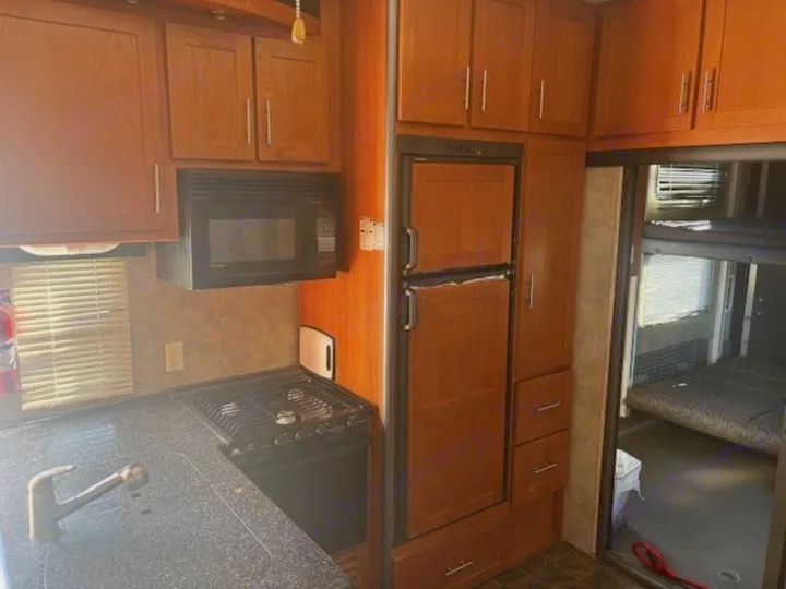 RV rental interior: kitchen with microwave, stove, sink, fridge, and adjacent sleeping area with a bed.. Keystone RV Fuzion Toy Hauler 2009