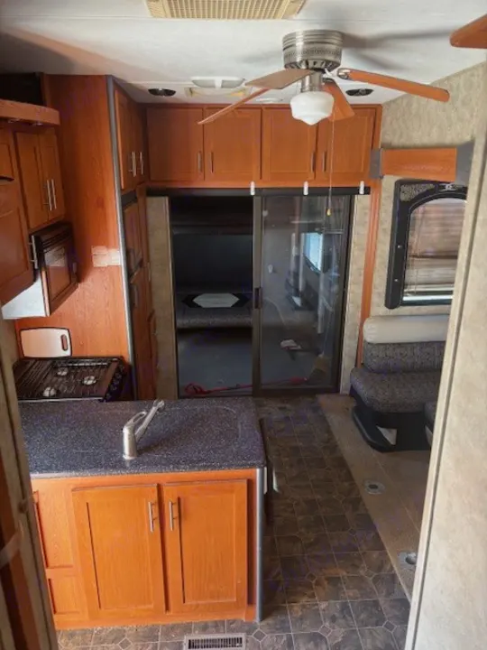 Interior of an rv rental featuring a kitchen with sink and wood cabinets, a ceiling fan, and a living area. Sliding doors lead to the back.. Keystone RV Fuzion Toy Hauler 2009