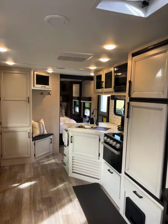 Bright rv rental interior with a modern kitchen, refrigerator, stove, and a glimpse of the integrated bedroom.. Jayco Jay Feather 2022