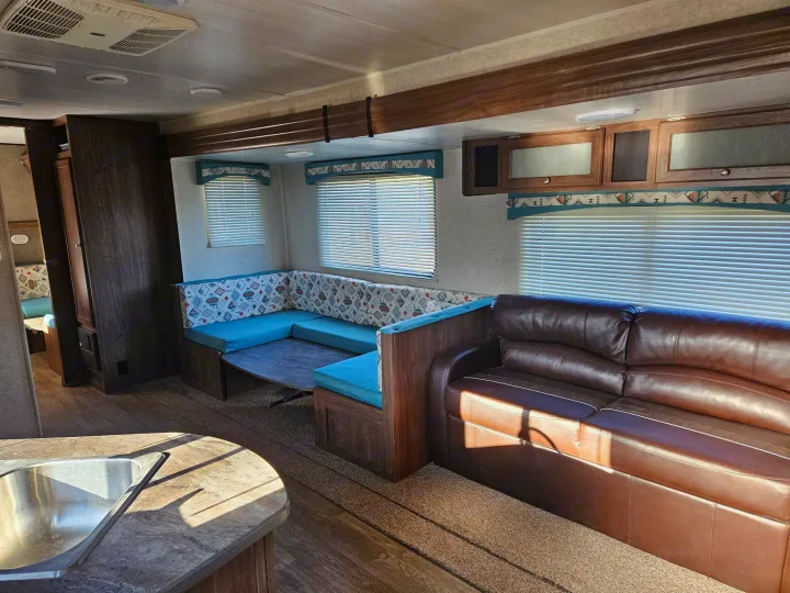 Comfortable RV rental living area with U-shaped dinette, brown sofa, and kitchen counter. Bright, modern interior.. Heartland RVs Prowler 2018