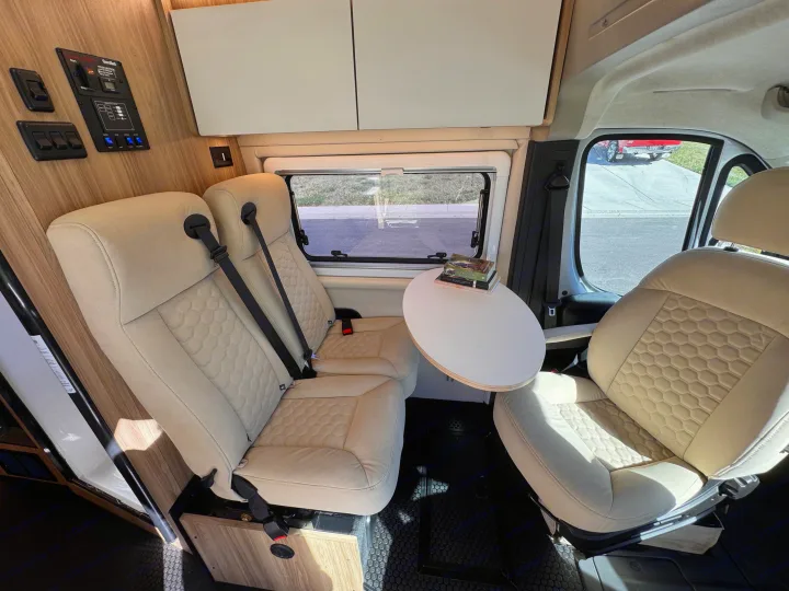 Modern RV rental interior: beige passenger seats, a small dining table, and a control panel for comfortable travel.. Forest River Coachmen Pixel 2026