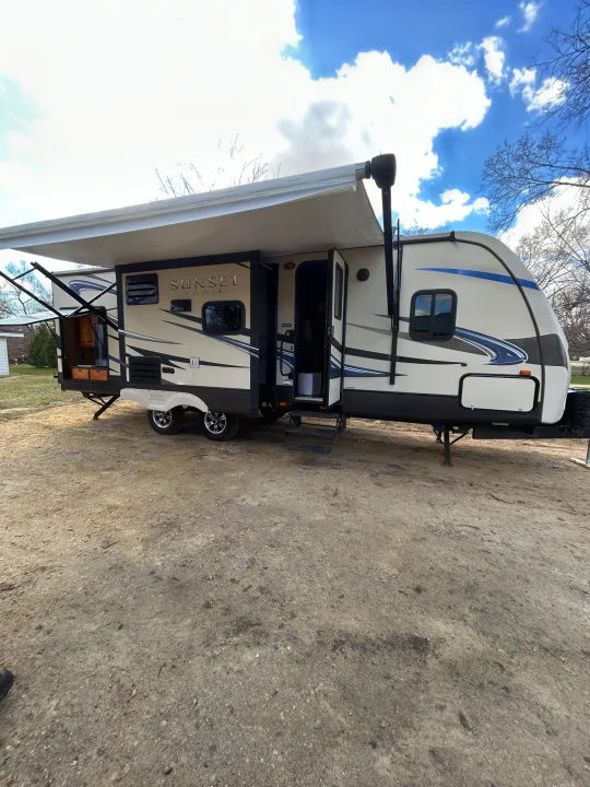 A beige and black Sunset Trail rv rental with an extended awning and outdoor kitchen is parked on gravel under a blue sky.. Crossroads RV Sunset Trail Reserve 2014