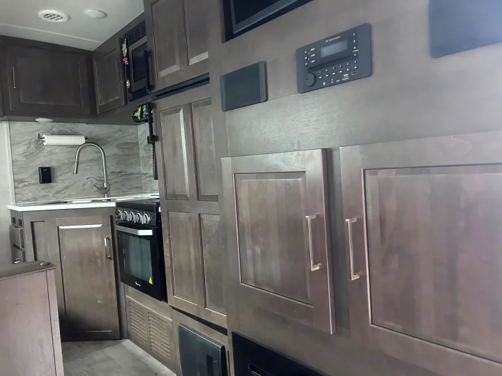 Modern RV rental interior: well-equipped kitchen with sink, stove, microwave, cabinets, and control panel.. Forest River Rockwood Ultra Lite 2021