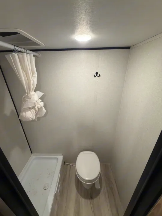 Compact RV rental bathroom features a toilet and shower stall with a tied-up curtain, optimizing small space.. Coleman 17B 2026