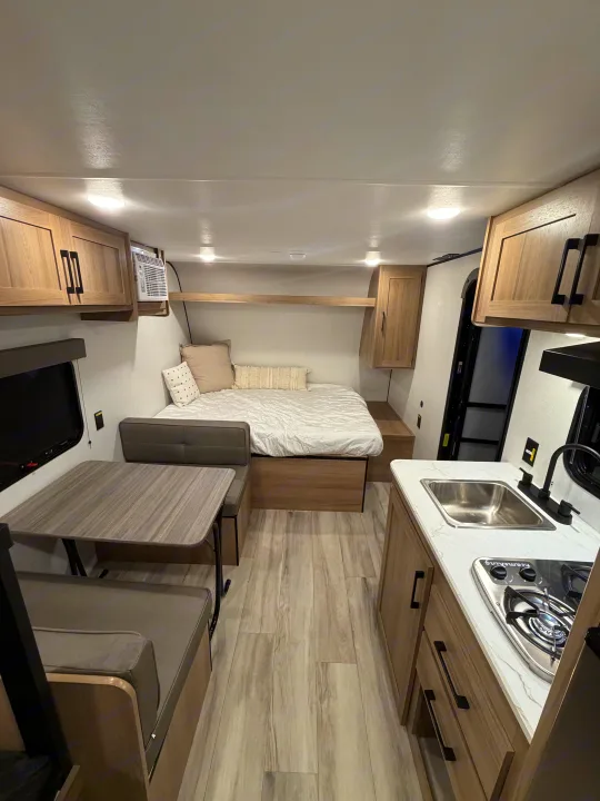Bright, modern rv rental interior showcasing a bed, kitchen, and dinette with stylish wood accents.. Coleman 17B 2026