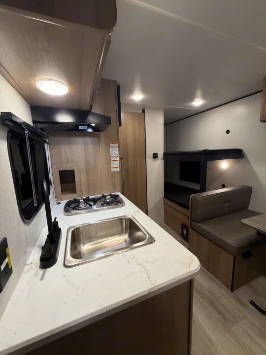 Inside this RV rental: a compact kitchen with a sink, stove, and a dinette with a bunk bed, ideal for travelers.. Coleman 17B 2026