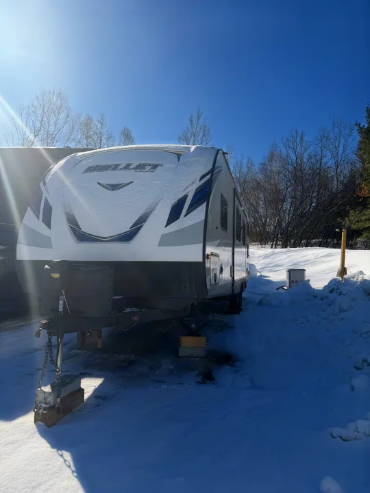 A white Bullet travel trailer (RV rental) covered in snow, parked under a bright blue winter sky.. Keystone RV Bullet Ultra Lite 2019