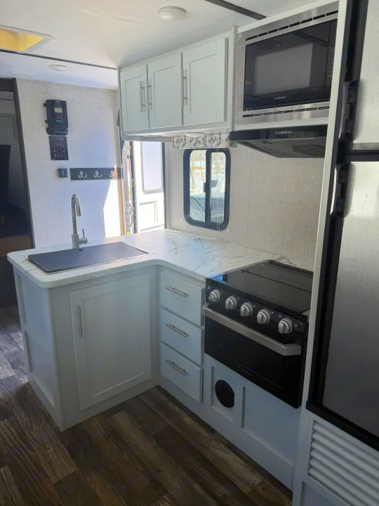 Modern rv rental kitchen featuring light gray cabinets, marble counters, a sink, stove, microwave, and integrated fridge.. Keystone RV Bullet Ultra Lite 2019