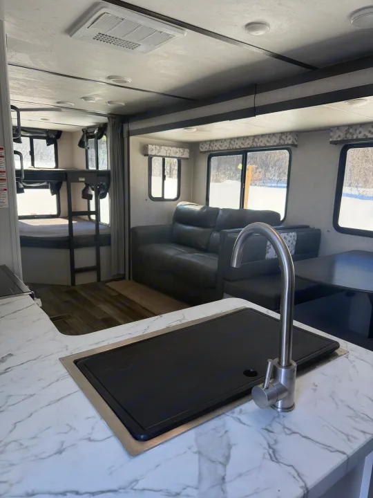 Inside a spacious RV rental: foreground shows a kitchen counter with a sink. Beyond are a sofa, dining area, and bunk beds.. Keystone RV Bullet Ultra Lite 2019