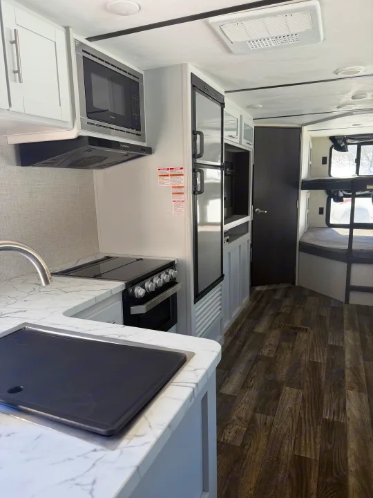 Bright RV rental interior: modern kitchen with microwave, stove, fridge, sink, marble counters, and bunk beds visible.. Keystone RV Bullet Ultra Lite 2019