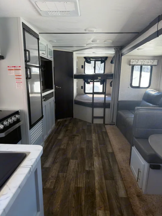 RV rental interior showcasing a modern kitchen, bunk beds, and cozy living area with sleek wood-look flooring.. Keystone RV Bullet Ultra Lite 2019