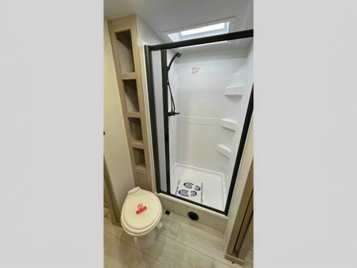 This RV rental bathroom features a glass-enclosed shower with a skylight, toilet, and convenient shelving.. Della Terra 250QB 2026