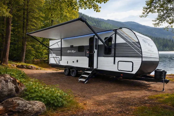 RV rental travel trailer with extended awning, parked by a scenic lake amidst mountains. Perfect for outdoor camping adventures.. Open Range Conventional 26BHS Travel Trailer 2025
