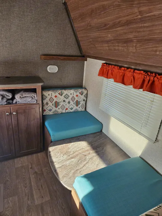 Cozy rv rental camper dinette with turquoise cushions, patterned backrest, wood accents, and window. Great for travel.. Heartland RVs Prowler 2018
