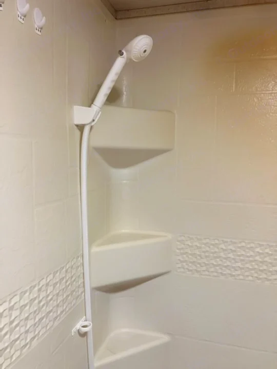 Compact shower in RV rental featuring handheld showerhead, multiple corner shelves, and textured paneling.. Heartland RVs Prowler 2018