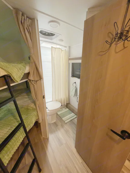 Compact RV rental interior: bunk beds with green blankets, a small bathroom with toilet, shower, and window.. Forest River Rockwood Mini Lite 2024