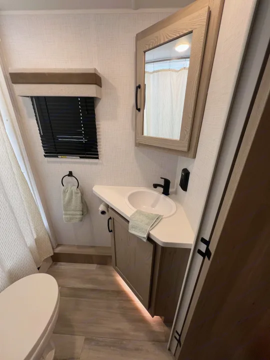 RV rental bathroom: compact design with corner sink, illuminated vanity, mirror, toilet & shower area.. Forest River Rockwood Mini Lite 2024