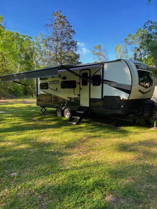 Modern Minilite travel trailer rv rental with extended awning, parked on a grassy site under a clear blue sky, ready for camping.. Forest River Rockwood Mini Lite 2024