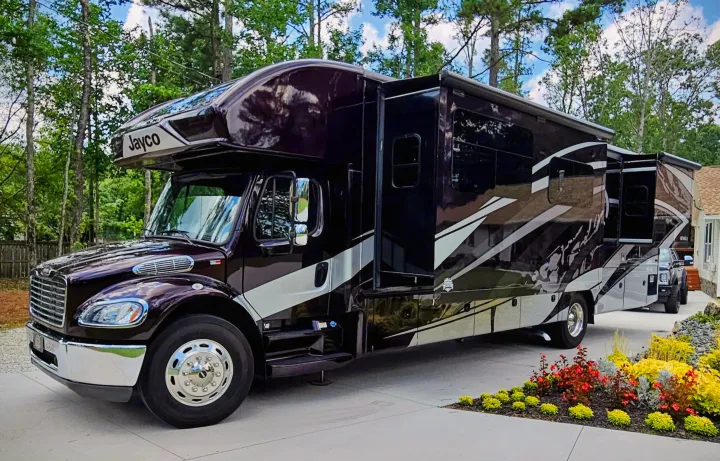 This dark Jayco Seneca RV, ideal for rv rental, is parked with slide-outs extended on a driveway, surrounded by trees.. Jayco Seneca 2021