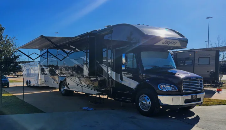 Spacious Jayco RV rental with awning extended, towing an enclosed trailer, parked under a clear blue sky at a campground.. Jayco Seneca 2021